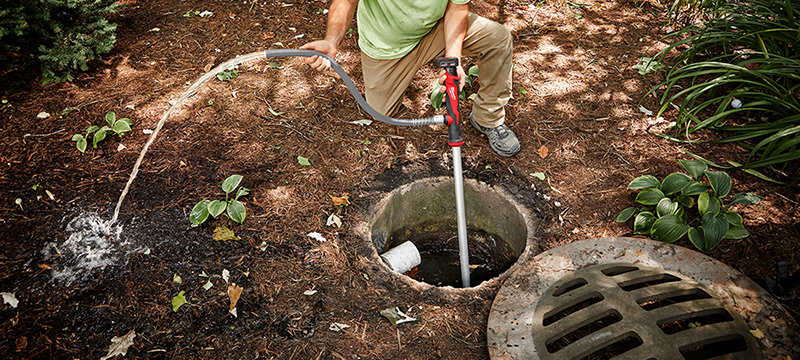 A Milwaukee M12 Stick Transfer Pump is used to pump water out of a sewage drain.