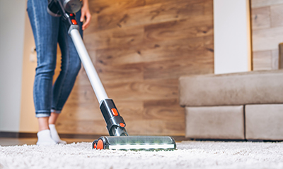 A woman cleans an area rug with a stick vacuum.