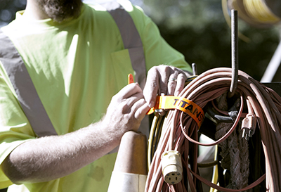 An orange TitanStrap strap is used to secure an electrical cord to a truck.