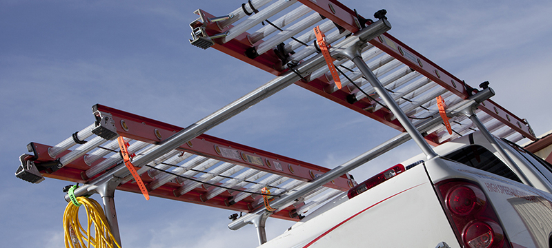 Several TitanStrap straps are used to secure ladders to a roof rack.