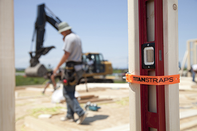 An orange TitanStrap strap is used to secure a level to a wall stud.