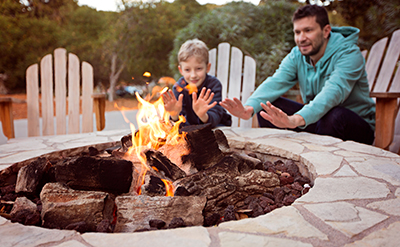 A father and son warm their hands around a fire pit.