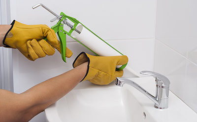 Sealant is applied between a wall and sink with a caulk gun.
