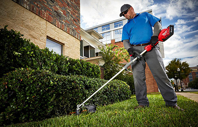 A Milwaukee battery-powered string trimmer is used to clean around bushes.