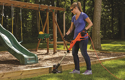 A Black and Decker electric string trimmer is used to cut around a playset.
