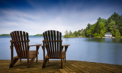 Two chairs on a deck overlooking a lake.