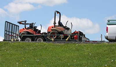 Two riding lawn mowers sit on a landscape trailer.