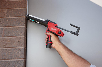 A Milwaukee M12 Caulk Gun is used to apply caulk on the edge of bricks.