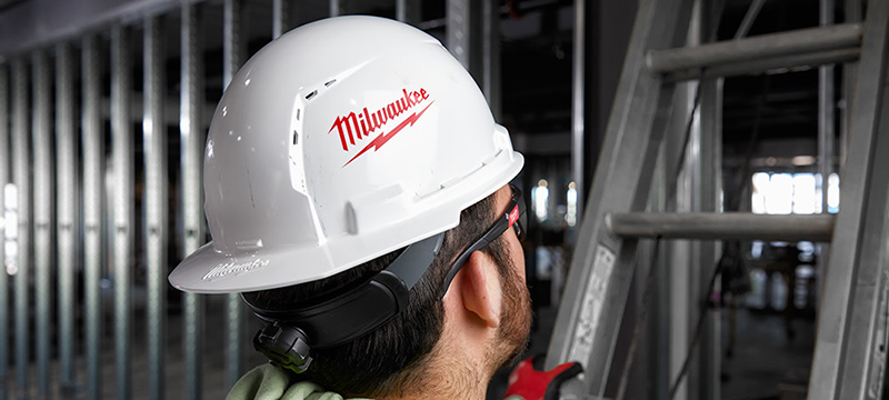 A worker wearing a Milwaukee Vented Type-1 Hard Hat prepares to climb a ladder.