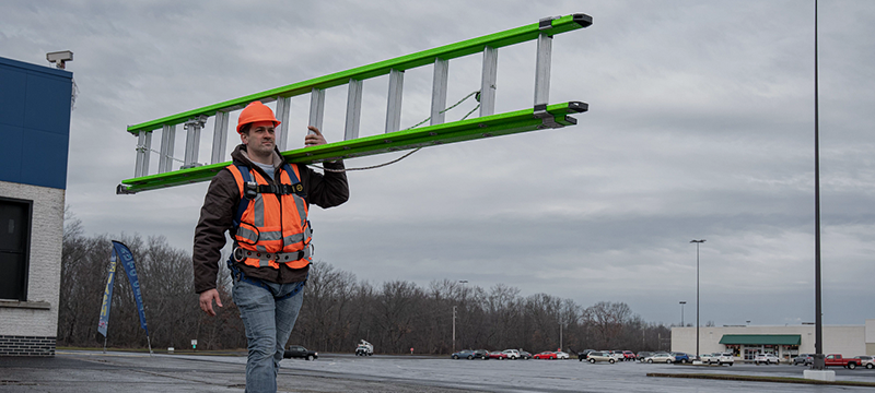A construction worker carries a Werner AERO 20-Foot Extension Ladder