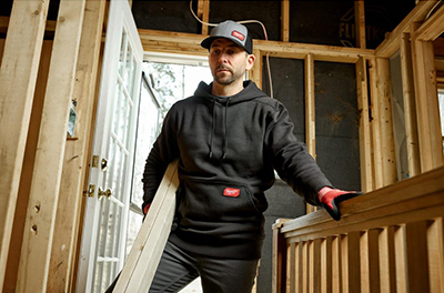 A man wears a black Milwaukee Midweight Pullover Hoodie while carrying lumber.