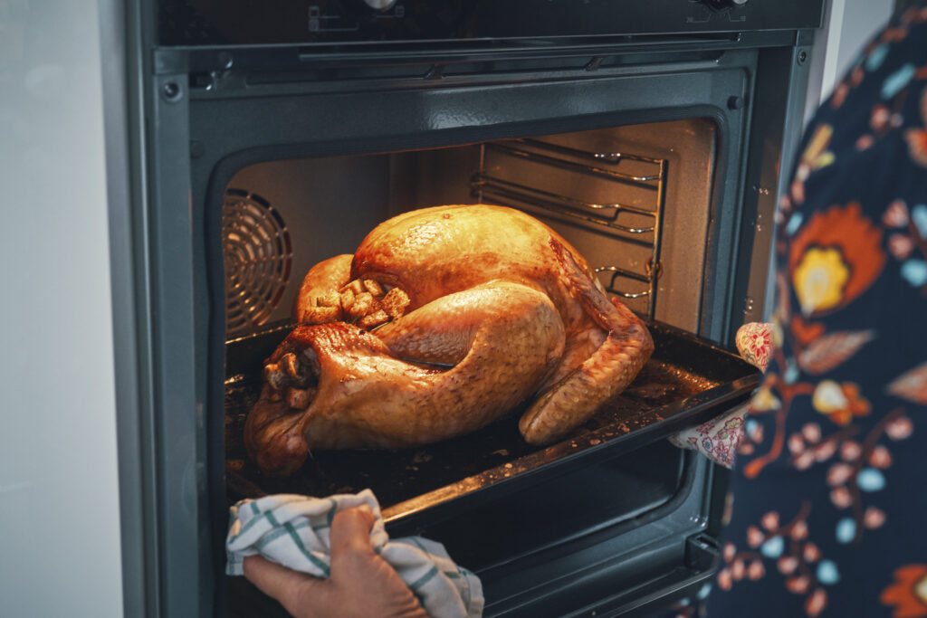 Person in colorful shirt removing cooked turkey from oven. 