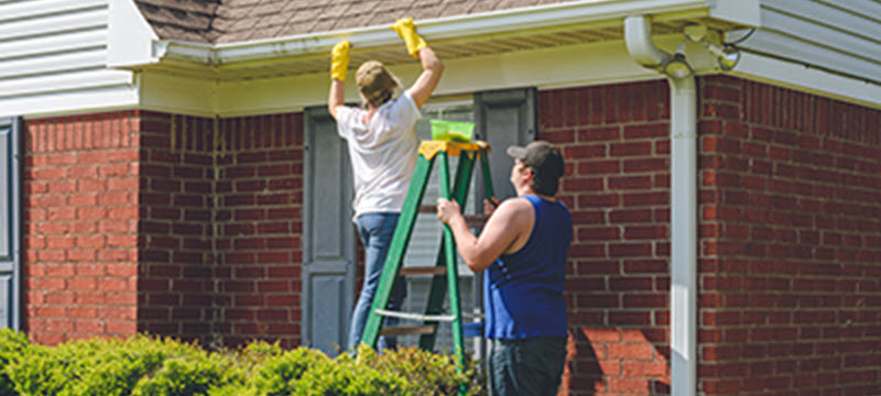 Woman on step ladder cleaning gutter