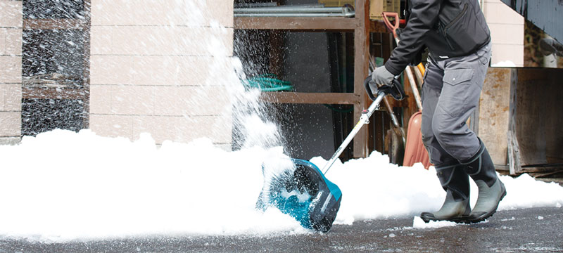 maintenance worker clearing a snow covered sidewalk with the Makita SN400MP Snow shovel attachment.